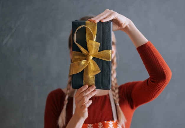 Mujer sosteniendo una caja con un regalo de Navidad en sus manos delante de su cara