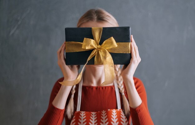 Mujer sosteniendo una caja con un regalo de Navidad en sus manos delante de su cara