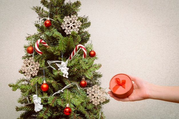 Mujer sosteniendo una caja de regalo redonda roja en la mano, decorando el árbol de Navidad con bolas, luces, decoración festiva. Navidad, decoraciones de año nuevo. concepto de vacaciones de invierno