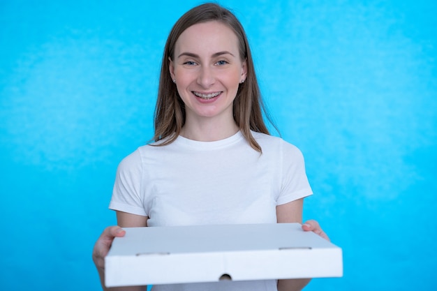 Mujer sosteniendo cajas de pizza sobre pared azul con expresión feliz