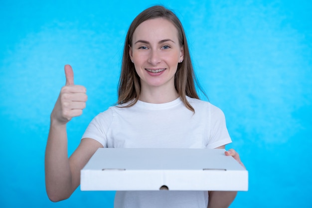 Mujer sosteniendo cajas de pizza sobre pared azul con expresión feliz