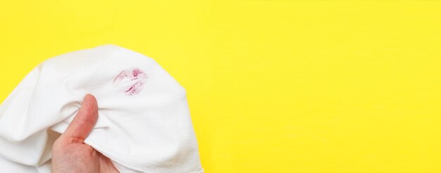 Mujer sosteniendo una camisa blanca con lápiz labial beso rojo sobre un fondo amarillo