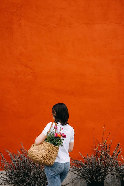 Mujer sosteniendo una canasta con flores de ranúnculo rosa junto a una gran pared naranja