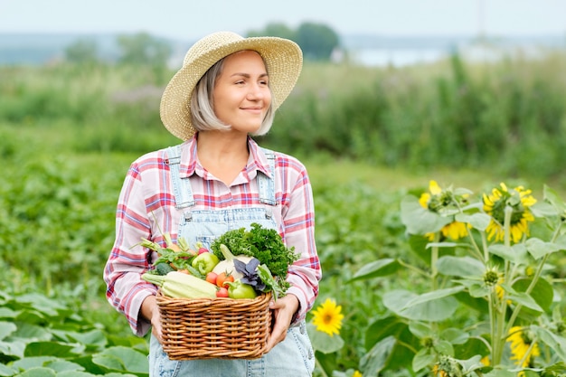 Mujer sosteniendo una canasta llena de cosecha de hortalizas orgánicas y raíz en Organic Bio Farm. Cosecha de hortalizas de otoño.