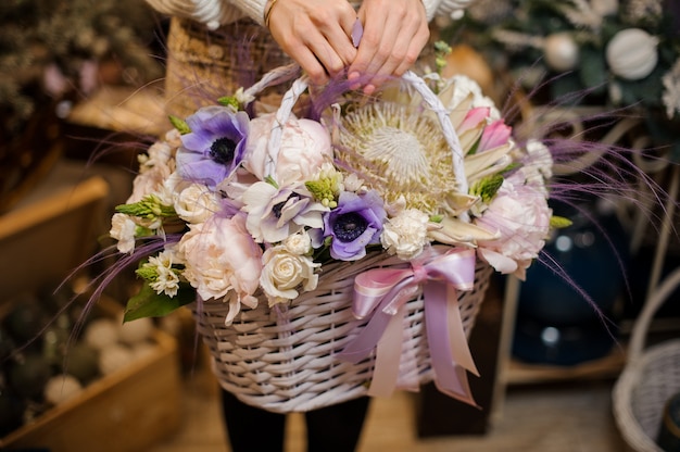 Mujer sosteniendo una canasta de mimbre de tiernas flores blancas, rosadas y púrpuras