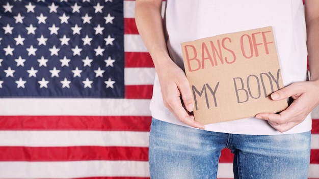 Mujer sosteniendo un cartel Prohibición de mi cuerpo Bandera estadounidense en el fondo Protesta contra la ley contra el aborto