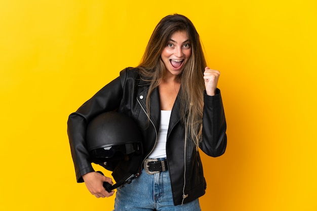 Mujer sosteniendo un casco de moto aislado en amarillo celebrando una victoria en posición ganadora