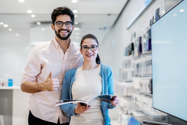 Mujer sosteniendo el catálogo y el hombre da pulgares mientras están de pie en la tienda de tecnología. Tecnologías contemporáneas.