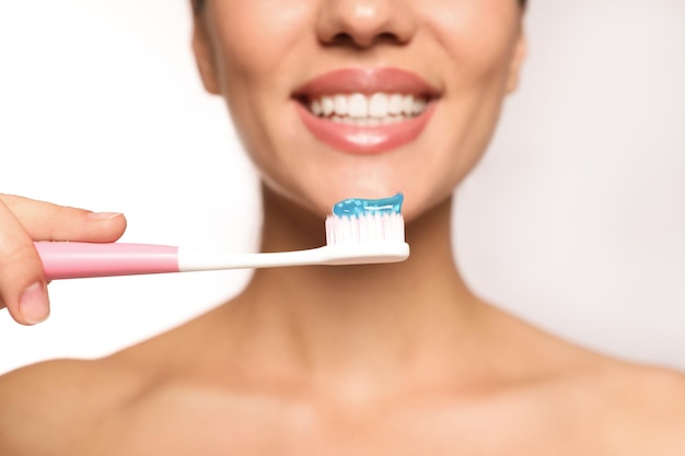 Mujer sosteniendo cepillo de dientes con pasta en primer plano de fondo claro