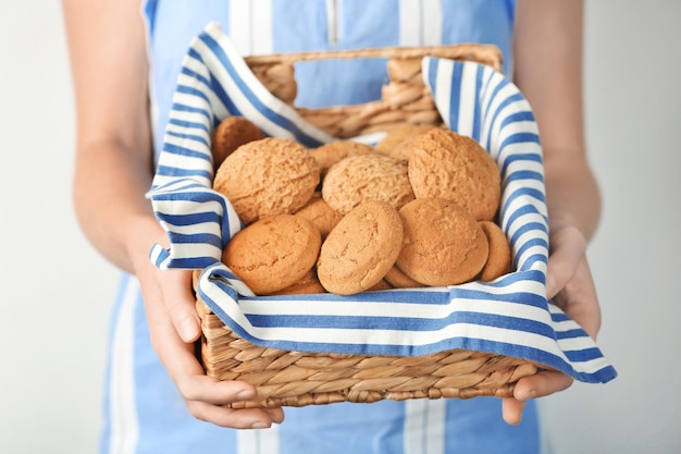 Mujer sosteniendo una cesta de mimbre con galletas de avena sobre un fondo claro