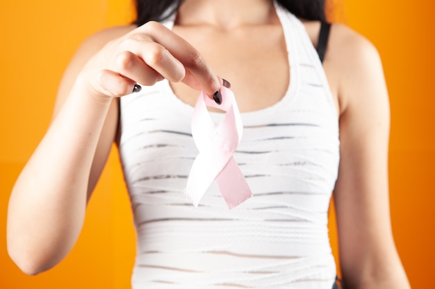 Mujer sosteniendo cinta rosa sobre fondo naranja