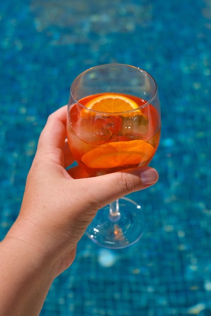 Mujer sosteniendo cóctel aperol spritz en la fiesta de verano junto a la piscina Concepto de celebración del evento