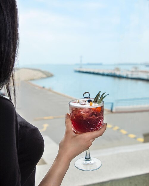 Mujer sosteniendo un cóctel con vista al mar en el restaurante