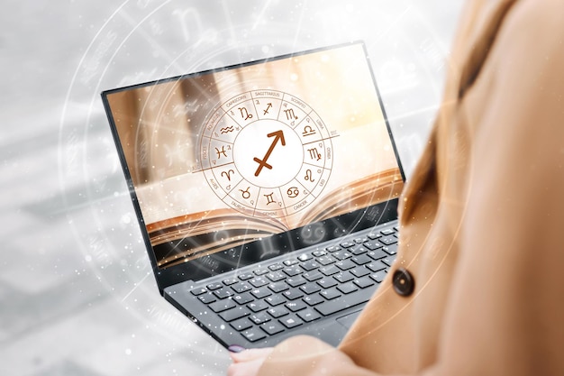 Mujer sosteniendo una computadora portátil abierta con una imagen de un libro y el círculo zodiacal
