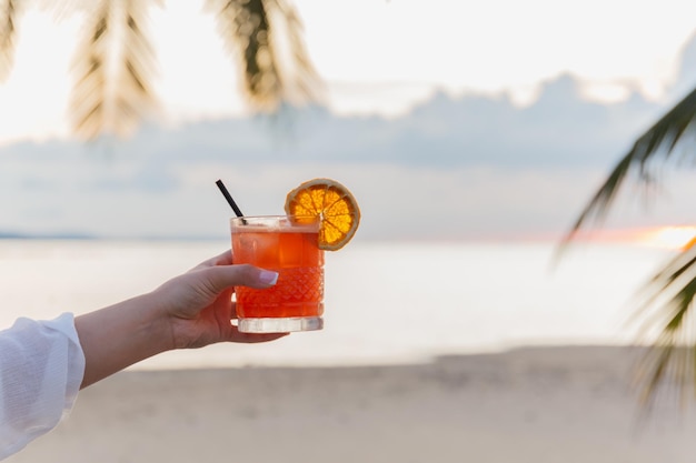 Mujer sosteniendo una copa de cóctel en la playa al atardecer