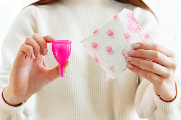 Mujer sosteniendo la copa menstrual en una mano y la almohadilla médica en otra de cerca