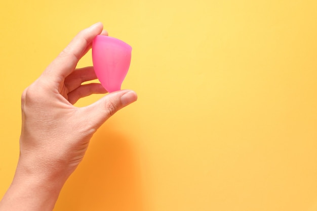 Mujer sosteniendo la copa menstrual en la mano sobre un fondo amarillo