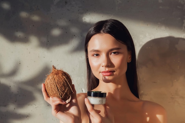 Mujer sosteniendo crema cosmética y coco para aplicar en la piel de la cara