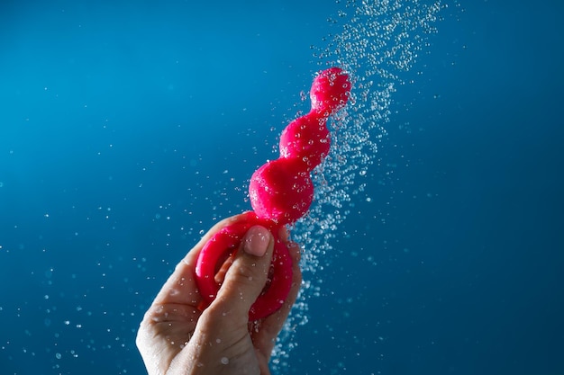 Mujer sosteniendo cuentas anales rosadas bajo agua corriente sobre fondo azul concepto de higiene de juguetes sexuales