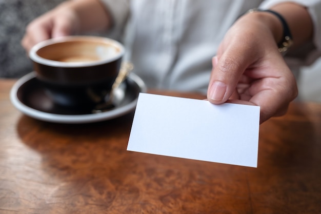 Una mujer sosteniendo y dando una tarjeta de presentación vacía en blanco a alguien mientras bebe café