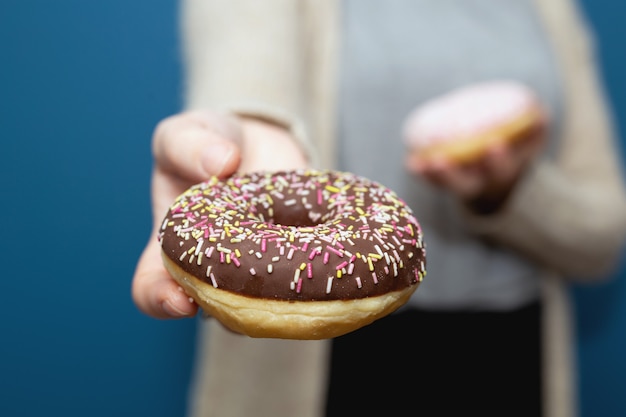 Mujer sosteniendo una deliciosa dona colorida con chispas y regalando la dona, compartiendo