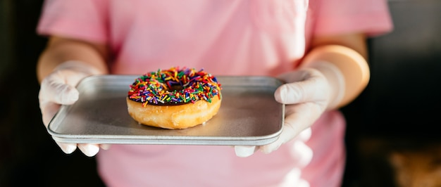 Mujer sosteniendo donut helado de chocolate fresco con chispitas sobre placa horneada.