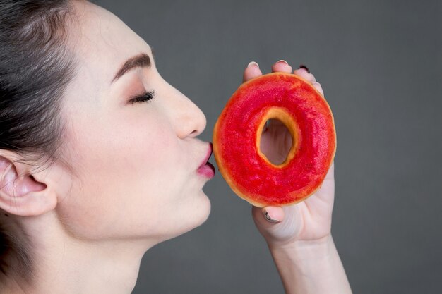 Mujer sosteniendo donut sobre fondo gris