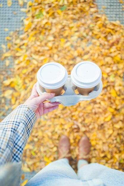 Foto una mujer sosteniendo dos tazas de café para llevar en otoño en la ciudad con ropa vintage.