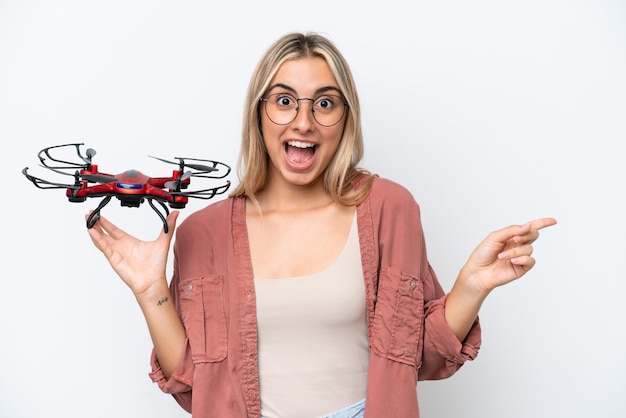 Mujer sosteniendo un dron sobre un fondo aislado sorprendida y señalando con el dedo hacia un lado