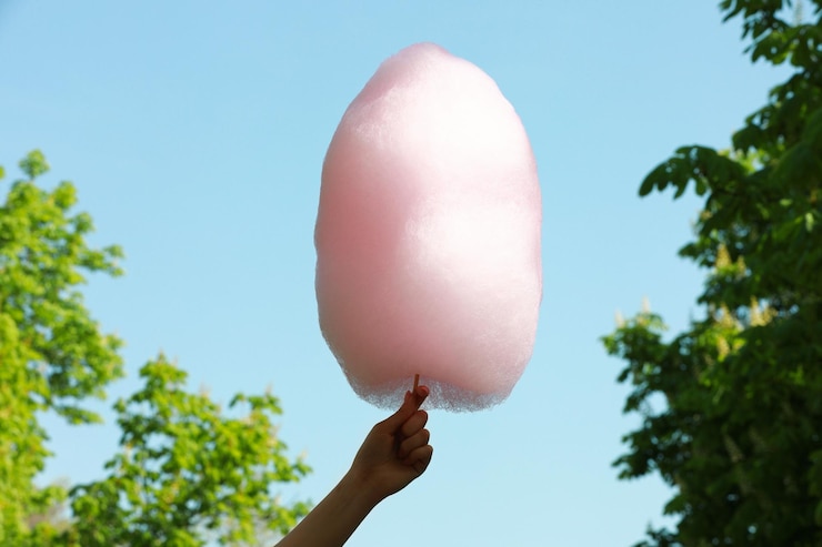 Foto mujer sosteniendo un dulce algodón de azúcar contra el cielo azul en primer plano
