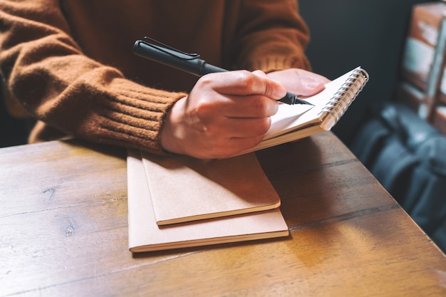 Una mujer sosteniendo y escribiendo en el cuaderno en blanco con pluma estilográfica en mesa de madera