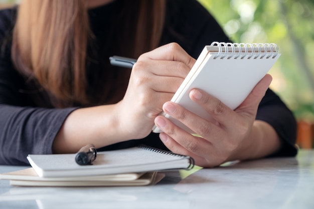 Una mujer sosteniendo y escribiendo en el cuaderno mientras está sentado en la cafetería