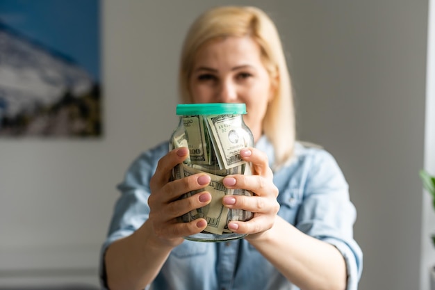 mujer sosteniendo un frasco transparente lleno de dólares americanos. Concepto de compras.