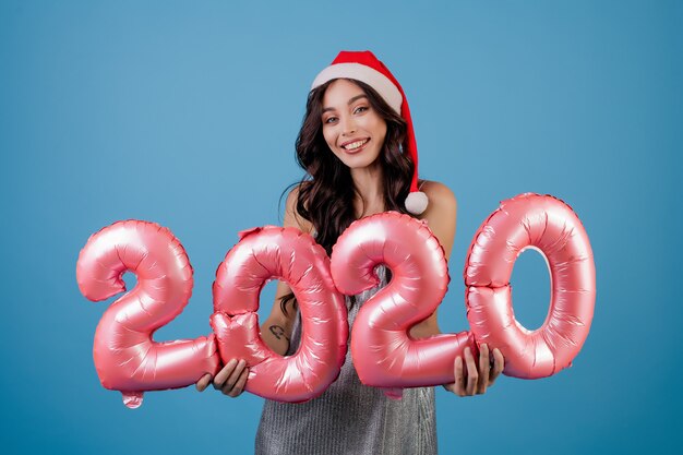 Mujer sosteniendo globos de año nuevo con vestido y sombrero de santa