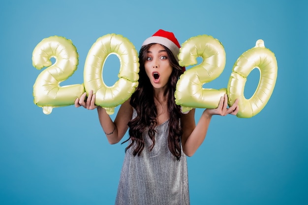 Mujer sosteniendo globos de año nuevo con vestido y sombrero de santa