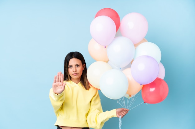 Mujer sosteniendo globos en una fiesta haciendo gesto de parada con su mano