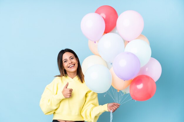 Mujer sosteniendo globos en una fiesta sobre la pared azul dando un gesto de pulgares arriba