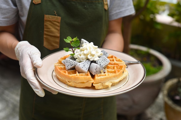 Mujer sosteniendo gofres belgas con fruta de dragón y helado en un plato