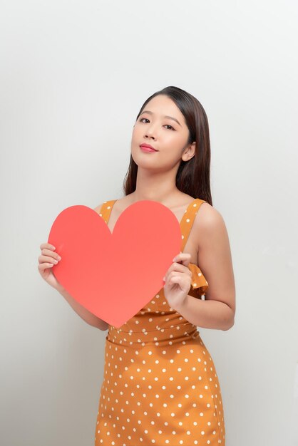 Mujer sosteniendo gran corazón rojo sobre fondo blanco.