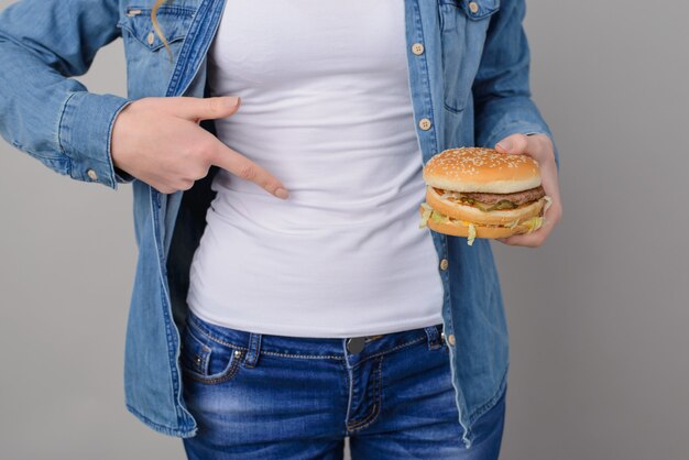 Mujer sosteniendo hamburguesa y apuntando sobre el estómago