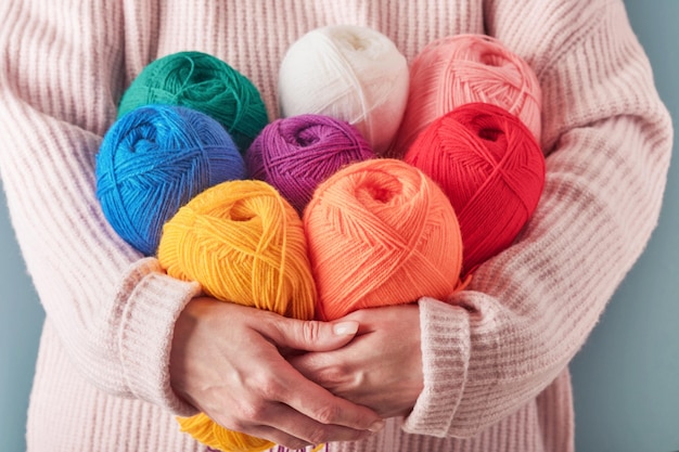Mujer sosteniendo hilos de lana coloridos o multicolores sobre fondo azul Muchas bolas multicolores de hilos closeup Costura o concepto de tejer