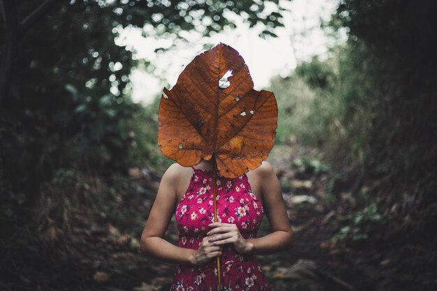 Foto mujer sosteniendo una hoja seca mientras está de pie en el campo