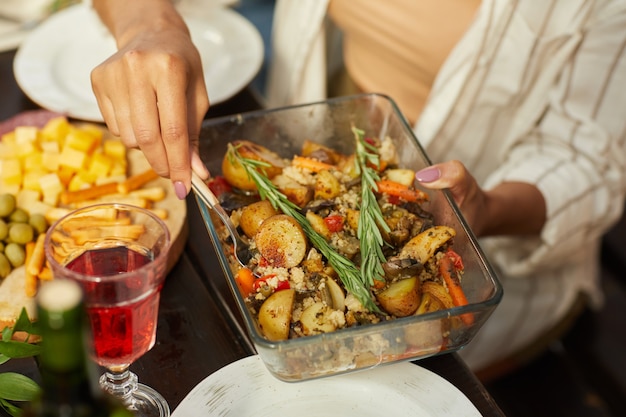 Mujer sosteniendo irreconocible plato con patatas asadas doradas mientras disfruta de una cena con amigos y familiares al aire libre