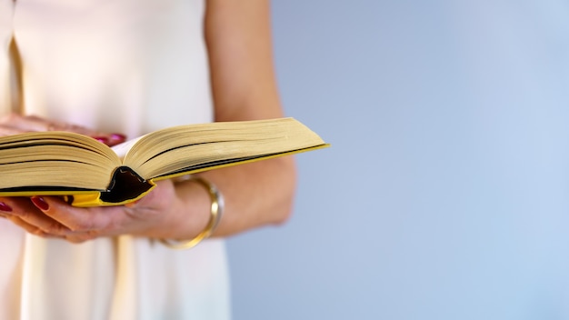 Mujer sosteniendo un libro y leyendo en postura de pie sobre la pared azul con espacio de copia.