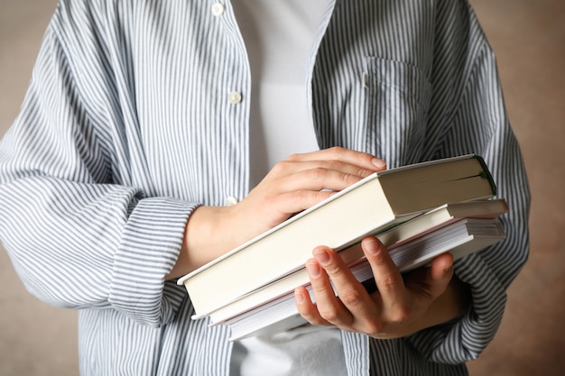 Mujer sosteniendo libros contra el espacio marrón, vista frontal