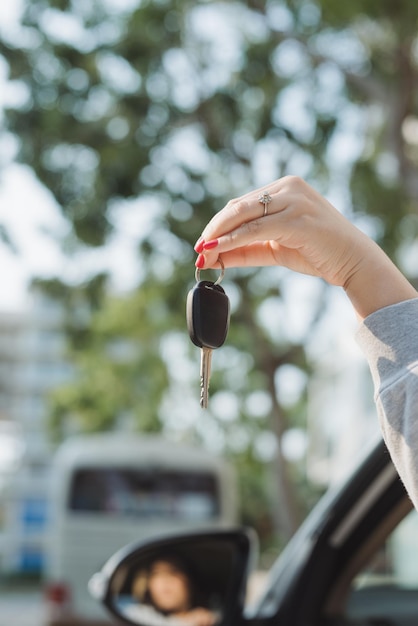 Mujer sosteniendo las llaves de encendido de un coche en su mano colgando a través de la ventana lateral abierta