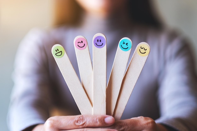 Una mujer sosteniendo una mano colorida dibuja caras de emoción feliz en un palo de madera