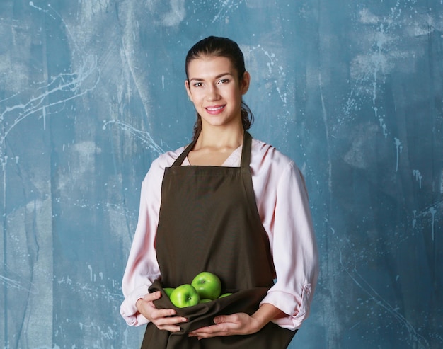 Mujer sosteniendo manzanas en delantal sobre fondo de color