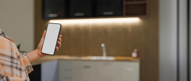 Una mujer sosteniendo una maqueta de teléfono inteligente sobre un espacio de cocina borroso en el fondo