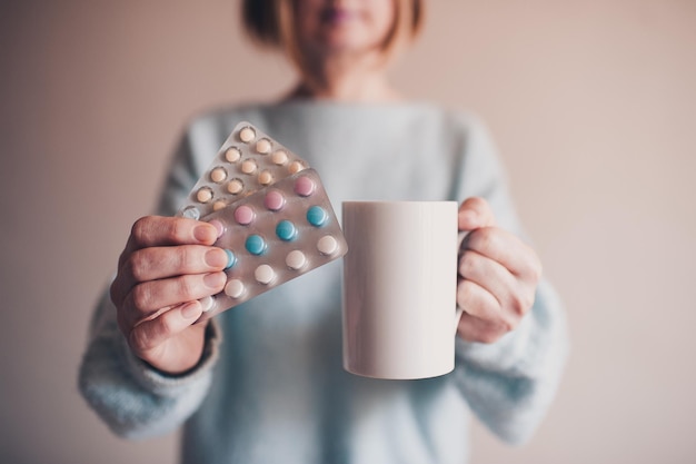 Mujer sosteniendo medicamentos y una taza de té caliente